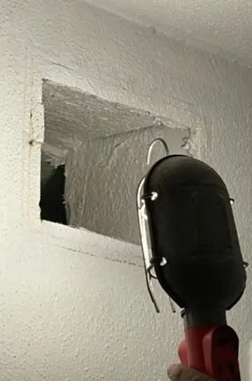 Work light held up to a ceiling register cut-out before a duct is cleaned