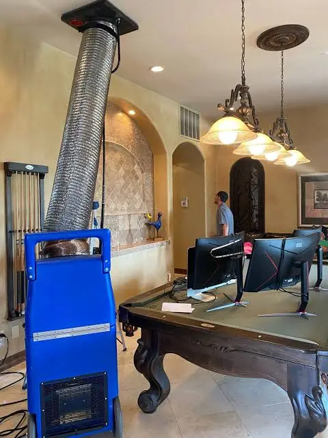 Blue negative-air machine with its ribbed trunk running up to an open ceiling register