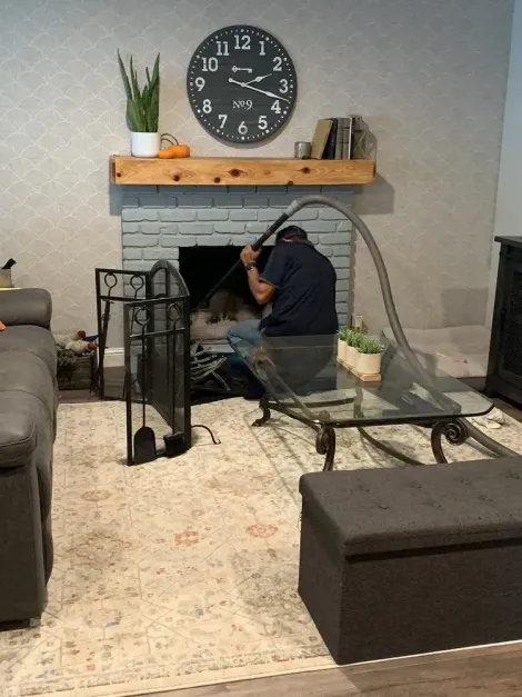 Technician vacuuming inside a painted brick fireplace in a living room