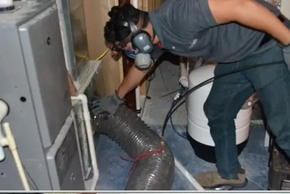 Technician in a respirator working the dryer duct behind the machine