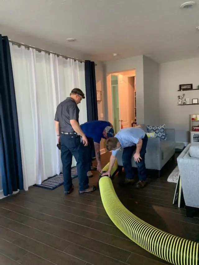 Three ABC crew laying a yellow suction hose across a client's living room floor