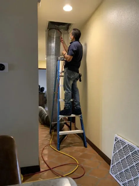 Technician on a stepladder working at a ceiling duct, a filter at the foot of the wall